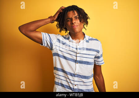 Afro american man with dreadlocks wearing striped shirt over isolated yellow background confuse and wonder about question. Uncertain with doubt, think Stock Photo