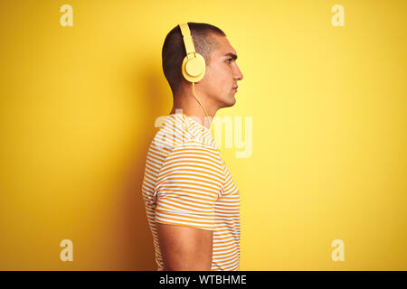 Young handsome man using headphones over yellow isolated background looking to side, relax profile pose with natural face with confident smile. Stock Photo