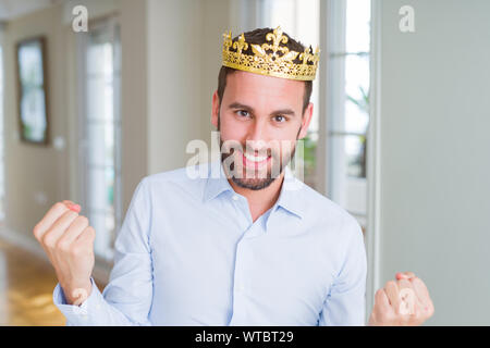 Handsome business man wearing golden crown as a king or prince celebrating surprised and amazed for success with arms raised and open eyes. Winner con Stock Photo