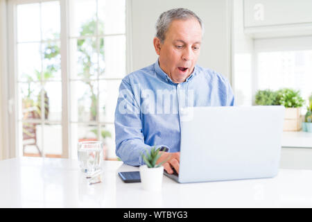 Handsome senior man using computer laptop working on internet scared in shock with a surprise face, afraid and excited with fear expression Stock Photo