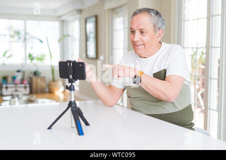 Handsome senior man doing video conference talking to the smartphone camera amazed and smiling to the camera while presenting with hand and pointing w Stock Photo