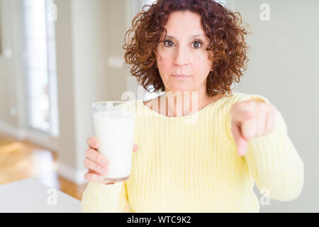 Senior woman drinking a glass of fresh milk pointing with finger to the camera and to you, hand sign, positive and confident gesture from the front Stock Photo