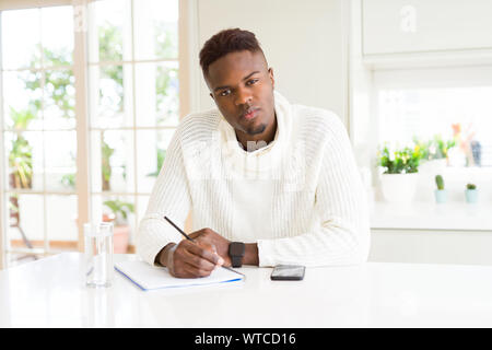 African american student man writing on a paper using a pencil with a confident expression on smart face thinking serious Stock Photo