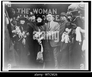 Mildred Harris Chaplin, full-length portrait, standing in crowd, facing front, guarded by a policeman, at a theater showing her film The Woman in His House (1920). Stock Photo