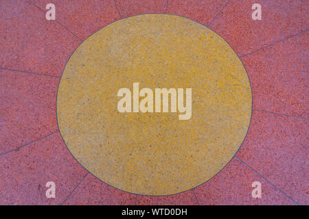 Background of terrazzo flooring in a pattern of red surrounding a circle of yellow. Terrazzo consists of chips of stone, glass, or other materials, he Stock Photo