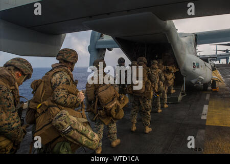 Marines with Echo Company, Battalion Landing Team, 2nd Battalion, 1st Marines, 31st Marine Expeditionary Unit, load onto an MV-22B Osprey tiltrotor aircraft as part of a simulated airfield seizure during a long-range raid from the amphibious assault ship USS Wasp (LHD 1), Philippine Sea, Aug. 12, 2019. The 31st MEU and Amphibious Squadron 11, aboard Wasp Amphibious Ready Group ships, conducted a series of sequential operations which simulated naval expeditionary combined-arms maneuver from amphibious assets to shore, utilizing Marine Air-Ground Task Force capabilities integrated across all war Stock Photo