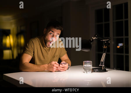 Young handsome man studying at home , using smartphone, surprise face looking at the camera Stock Photo