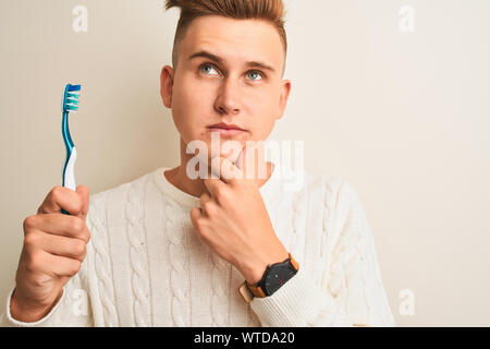 Young handsome man holding tooth brush standing over isolated white background serious face thinking about question, very confused idea Stock Photo