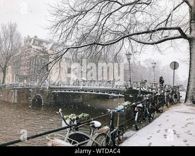Snowy bicycles on the bridge in the city center Amsterdam Netherlands. Blizzard on winter in the Netherlands. Bicycles covered with snow on a bridge. Stock Photo