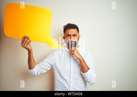 Young arab indian hispanic man holding speech bubble over isolated white background serious face thinking about question, very confused idea Stock Photo