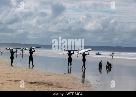Surfers carrying boards walk down beach at Saunton Sands, near Croyde, North Devon, England UK Stock Photo