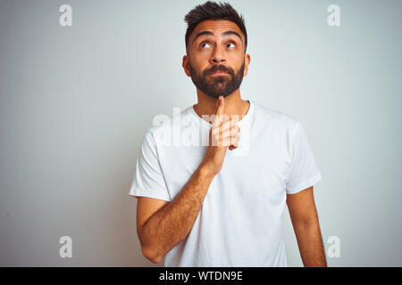 Young indian man wearing t-shirt standing over isolated white background Thinking concentrated about doubt with finger on chin and looking up wonderin Stock Photo