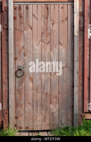 Red wooden old door in the fence with iron hinges and a round handle. The paint is faded. A lot of knots, bolts, nails. Vertical frame. Stock Photo