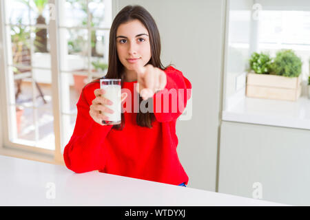 Beautiful young woman drinking a glass of fresh milk pointing with finger to the camera and to you, hand sign, positive and confident gesture from the Stock Photo