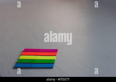 A set of colored bookmarks lies on a light colored surface from the bottom left. Stripe stickers. Red, yellow, green, blue. Selective focus. Stock Photo