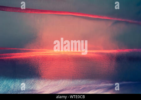 Abstract blurred background. Very colorful thin airy beautiful fabric with tints of red and blue. Texture of tulle in the sun at sunset. Shallow depth Stock Photo