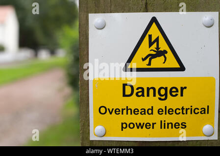 Danger overhead electrical power lines warning sign on wooden post with out of focus background Stock Photo