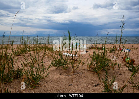 Empty used dirty plastic bottles on a sandy shore. Environmental pollution. Ecological problem. The end of the season. Marine pollution: plastic waste Stock Photo