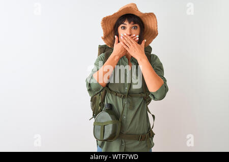 Hiker woman wearing backpack hat and water canteen over isolated white background shocked covering mouth with hands for mistake. Secret concept. Stock Photo