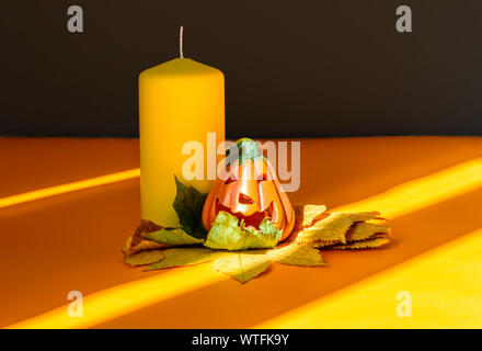 Ceramic Halloween pumpkin jack-o-lantern on dry autumn leaves, yellow candle and strong shadows Stock Photo
