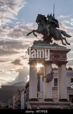 The Vercingetorix statue on a city square of Clermont Ferrand in France, sun setting and blasting sun rays behind it and Puy de Dome volcano Stock Photo