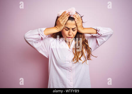 Young beautiful woman wearing pajama standing over pink isolated background suffering from headache desperate and stressed because pain and migraine.