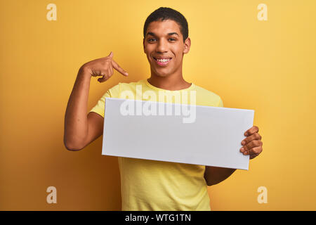 Young handsome arab man holding banner standing over isolated yellow background with surprise face pointing finger to himself Stock Photo