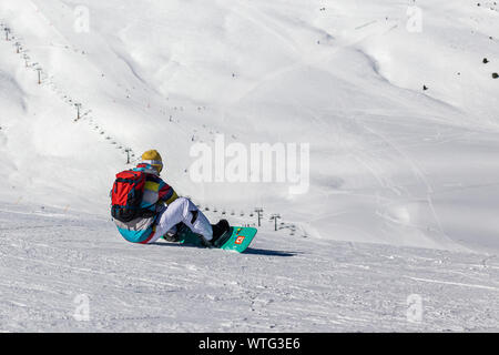 PYRENEES, ANDORRA - FEBRUARY 13, 2019: A snowboarder in bright clothes sits on a mountainside and prepares for the descent. Mountainsides and a lift l Stock Photo