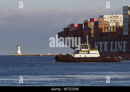 NYK Line container ship departing from the Port of Los Angeles as well as a tugboat and the Angeles Harbor Light. Stock Photo