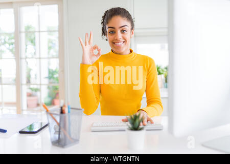 Young african american girl working using computer doing ok sign with fingers, excellent symbol Stock Photo