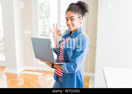 Young african american girl standing working using laptop doing ok sign with fingers, excellent symbol Stock Photo