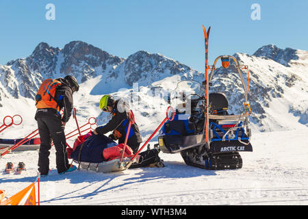 PYRENEES, ANDORRA - FEBRUARY 13, 2019: Rescuers at a ski resort prepare the victim for transportation. Two rescue workers lay the wounded on a sled ag Stock Photo