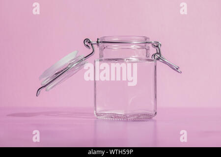 Empty glass jar with open lid and metal clasp on a pink background Stock Photo