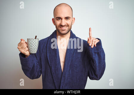 Young man wearing a bathrobe drinking a cup of coffee in the morning over isolated background surprised with an idea or question pointing finger with Stock Photo