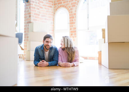 Young beautiful couple in love relaxing lying on the floor together with cardboard boxes around for moving to a new house Stock Photo