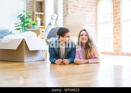 Young beautiful couple in love relaxing lying on the floor together with cardboard boxes around for moving to a new house Stock Photo
