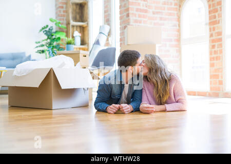 Young beautiful couple in love relaxing lying on the floor together with cardboard boxes around for moving to a new house Stock Photo