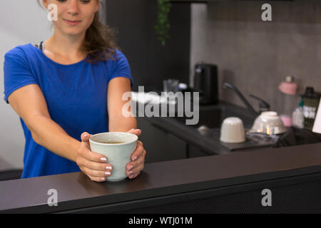 Female fitness assistant greeting you at homely gym bar with a cup of organic tea. Stock Photo