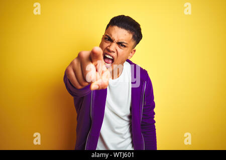 Young brazilian man wearing purple sweatshirt standing over isolated yellow background pointing displeased and frustrated to the camera, angry and fur Stock Photo