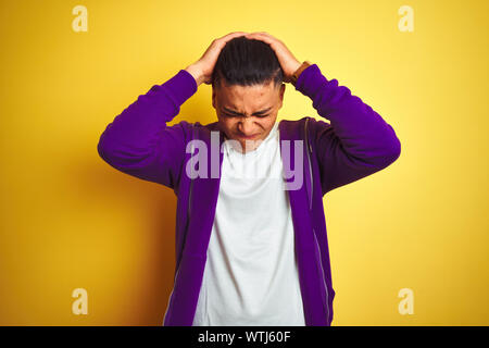 Young brazilian man wearing purple sweatshirt standing over isolated yellow background suffering from headache desperate and stressed because pain and Stock Photo