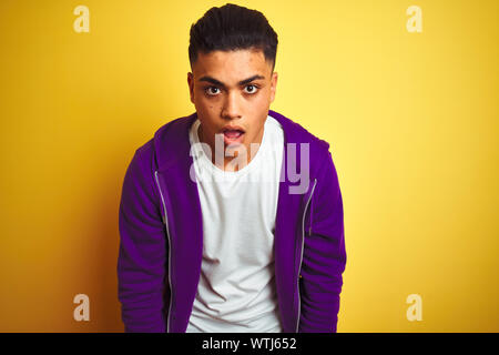 Young brazilian man wearing purple sweatshirt standing over isolated yellow background afraid and shocked with surprise and amazed expression, fear an Stock Photo