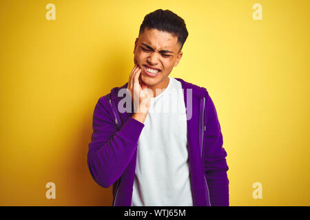 Young brazilian man wearing purple sweatshirt standing over isolated yellow background touching mouth with hand with painful expression because of too Stock Photo