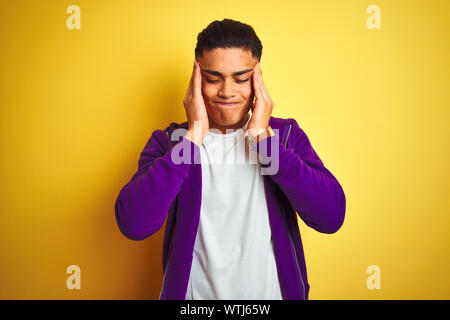 Young brazilian man wearing purple sweatshirt standing over isolated yellow background with hand on headache because stress. Suffering migraine. Stock Photo