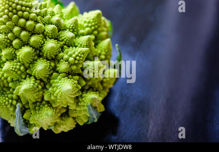 Close up view of amazing Romanesco broccoli or Roman cauliflower on wet dark blue background. Its form is a natural approximation of a fractal. Stock Photo
