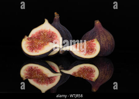 Group of two whole one half two slices of fresh fig fruit isolated on black glass Stock Photo