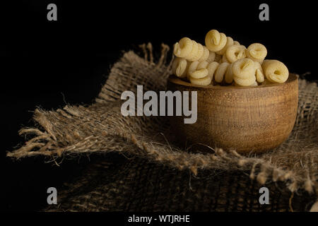 Lot of whole fresh raw pasta fusilli bucati in wooden bowl on jute cloth isolated on black glass Stock Photo