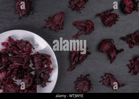 Lot of whole sweet red candied hibiscus on white ceramic plate flatlay on grey stone Stock Photo