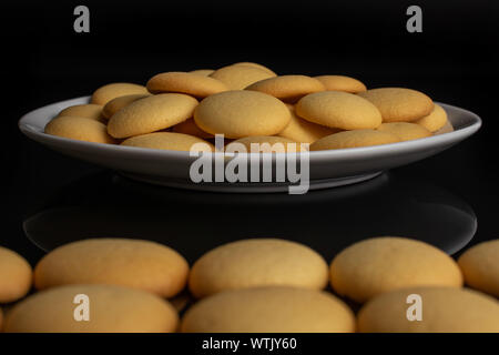 Lot of whole sweet golden sponge biscuit on white ceramic plate isolated on black glass Stock Photo