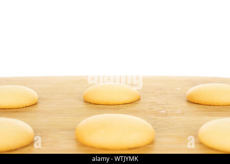 Group of six whole sweet golden sponge biscuit in closeup on bamboo cutting board isolated on white background Stock Photo