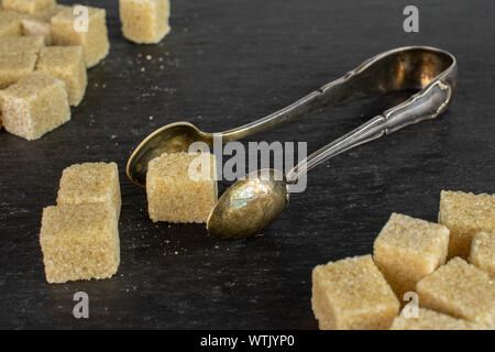 Lot of whole sweet brown sugar cube with sugar tongs on grey stone Stock Photo